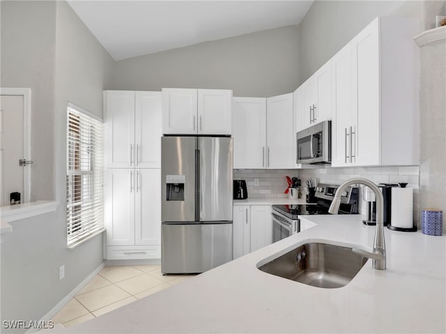 kitchen with lofted ceiling, appliances with stainless steel finishes, light tile patterned floors, and white cabinets