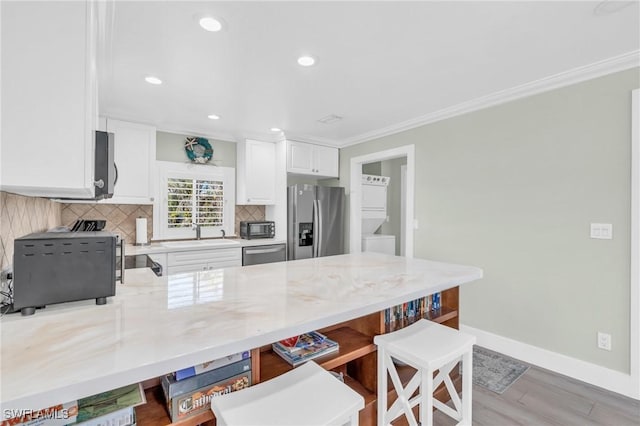 kitchen with appliances with stainless steel finishes, tasteful backsplash, white cabinetry, sink, and stacked washer and clothes dryer