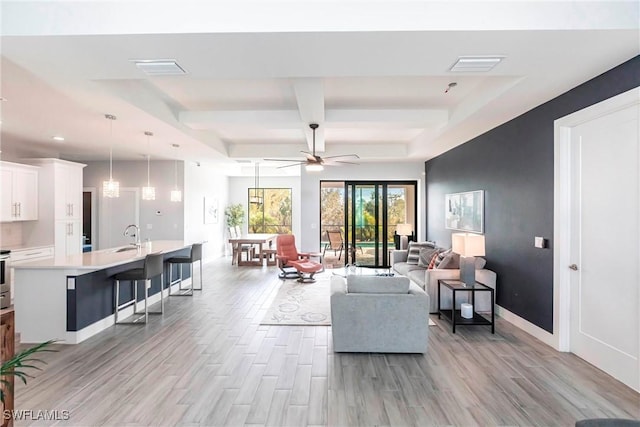 living room featuring coffered ceiling, sink, a raised ceiling, ceiling fan, and beam ceiling