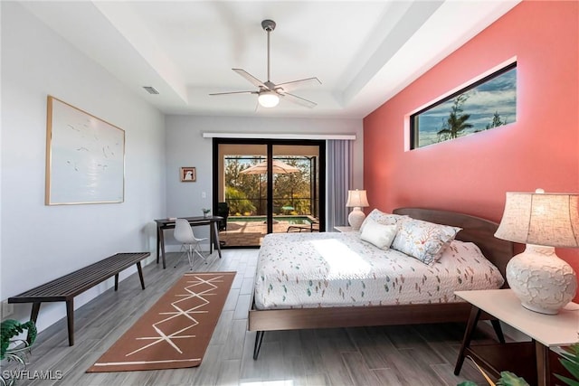 bedroom with access to exterior, hardwood / wood-style flooring, a raised ceiling, and ceiling fan