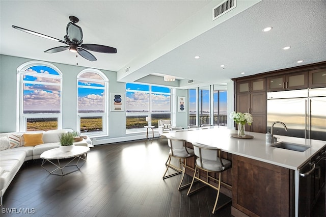 kitchen with a kitchen breakfast bar, dark hardwood / wood-style flooring, ceiling fan, dark brown cabinetry, and a center island with sink