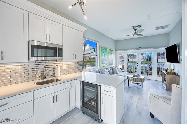 kitchen featuring sink, white cabinetry, wine cooler, tasteful backsplash, and kitchen peninsula