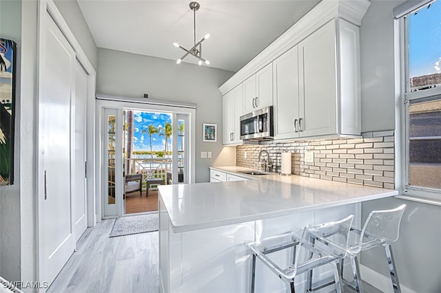 kitchen featuring pendant lighting, decorative backsplash, kitchen peninsula, and white cabinets