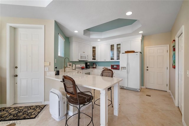 kitchen with white cabinetry, sink, kitchen peninsula, a raised ceiling, and white appliances