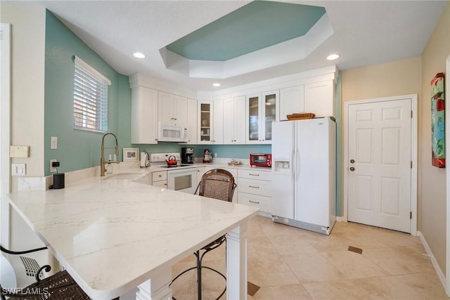 kitchen featuring white appliances, a kitchen breakfast bar, kitchen peninsula, white cabinets, and a raised ceiling