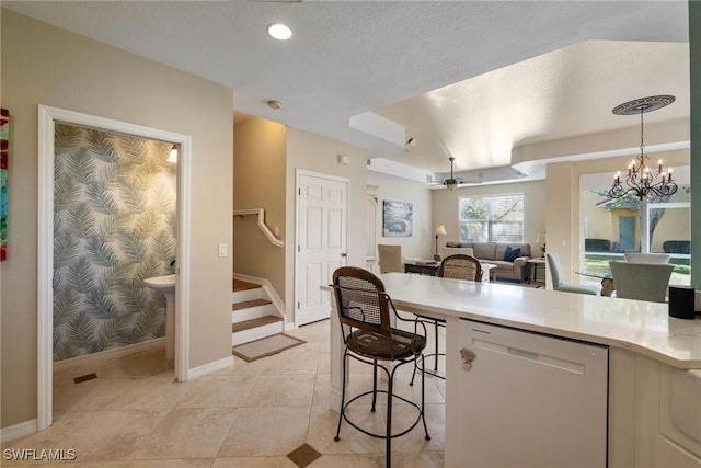 kitchen with light tile patterned flooring, ceiling fan with notable chandelier, pendant lighting, dishwasher, and a kitchen breakfast bar