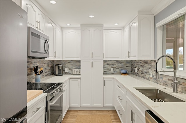 kitchen featuring white cabinetry, sink, backsplash, stainless steel appliances, and light wood-type flooring