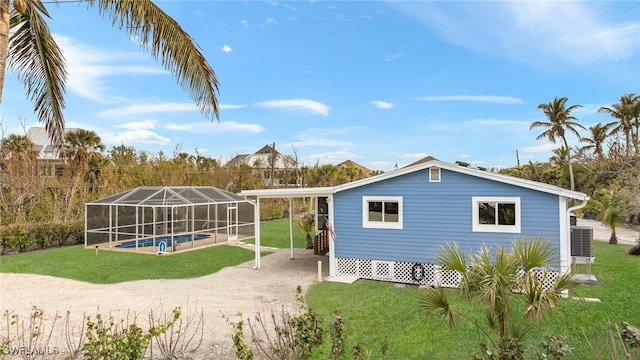 rear view of property with cooling unit, a lanai, and a lawn