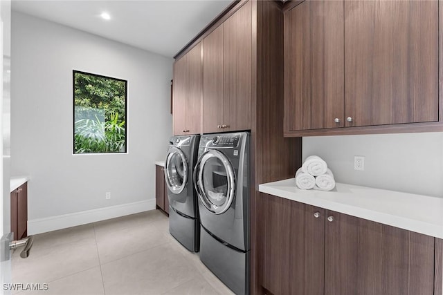 clothes washing area featuring washer and dryer, light tile patterned floors, and cabinets