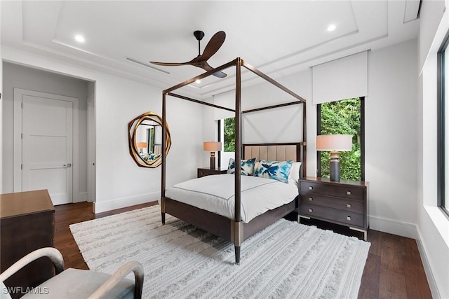 bedroom with ceiling fan, dark hardwood / wood-style floors, and a raised ceiling