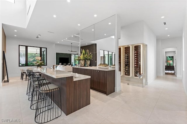 kitchen featuring a breakfast bar area, a high ceiling, dark brown cabinetry, beverage cooler, and a large island with sink