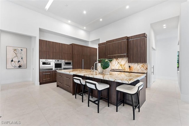 kitchen with stainless steel oven, a towering ceiling, a breakfast bar, and a spacious island