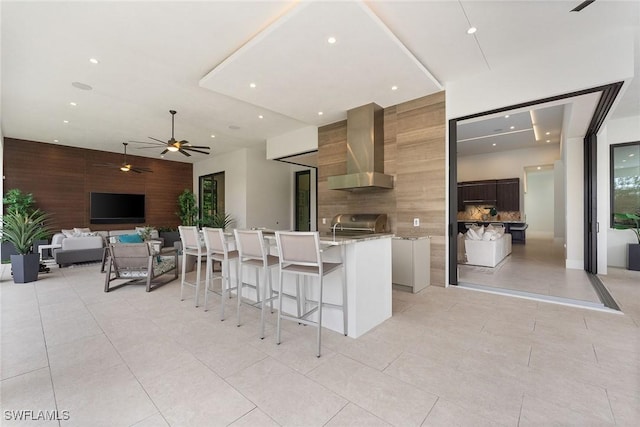 kitchen with a kitchen island, backsplash, a kitchen bar, light tile patterned floors, and wall chimney exhaust hood