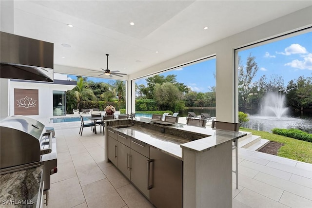 view of patio featuring area for grilling, sink, ceiling fan, and a water view