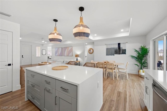 kitchen with pendant lighting, gray cabinetry, a tray ceiling, stainless steel dishwasher, and light wood-type flooring