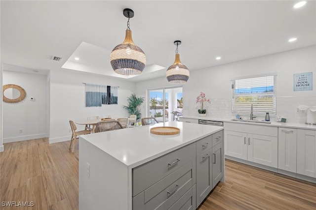 kitchen with sink, decorative light fixtures, a center island, a tray ceiling, and decorative backsplash