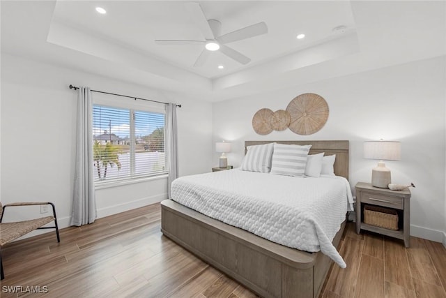 bedroom with a tray ceiling, ceiling fan, and light wood-type flooring