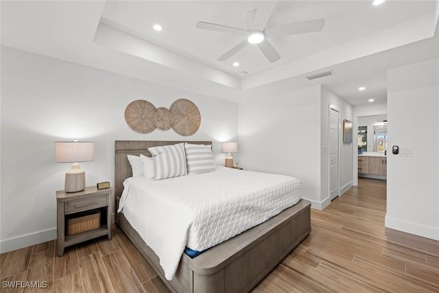 bedroom with ceiling fan, ensuite bathroom, a tray ceiling, and a closet