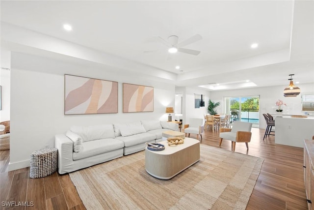 living room featuring a raised ceiling, hardwood / wood-style floors, and ceiling fan