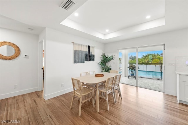 dining area with a raised ceiling and light hardwood / wood-style flooring