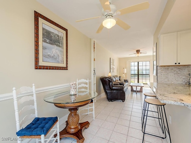 interior space with light tile patterned floors, a ceiling fan, and baseboards