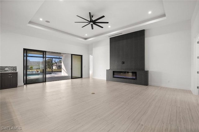 unfurnished living room featuring ceiling fan, a fireplace, a raised ceiling, and a high ceiling