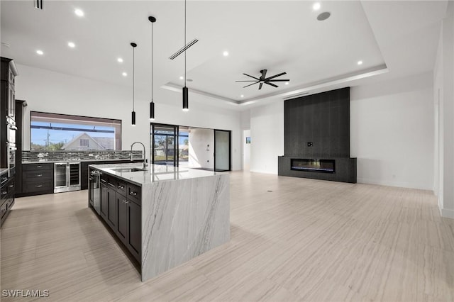 kitchen featuring a fireplace, sink, wine cooler, a large island, and a tray ceiling