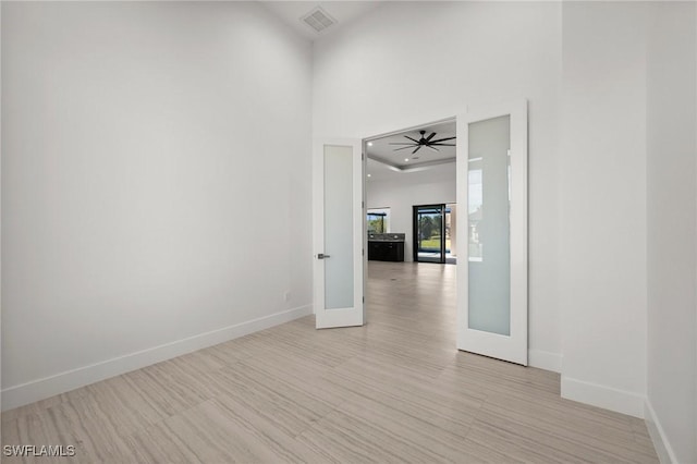 empty room featuring ceiling fan, a towering ceiling, light hardwood / wood-style floors, and french doors