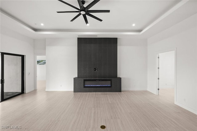 unfurnished living room featuring a tray ceiling, light hardwood / wood-style flooring, and a towering ceiling