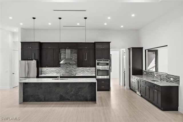 kitchen featuring pendant lighting, stainless steel appliances, wall chimney exhaust hood, and a center island with sink