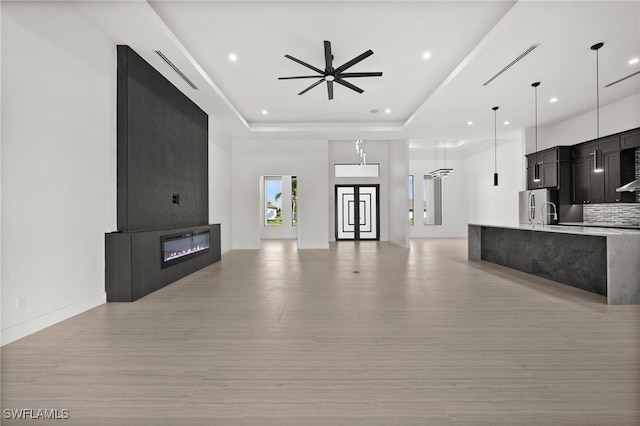 unfurnished living room with a tray ceiling, light hardwood / wood-style flooring, a large fireplace, and ceiling fan