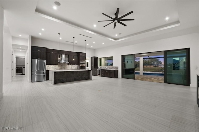 kitchen with a kitchen island, a tray ceiling, stainless steel refrigerator, and wall chimney exhaust hood