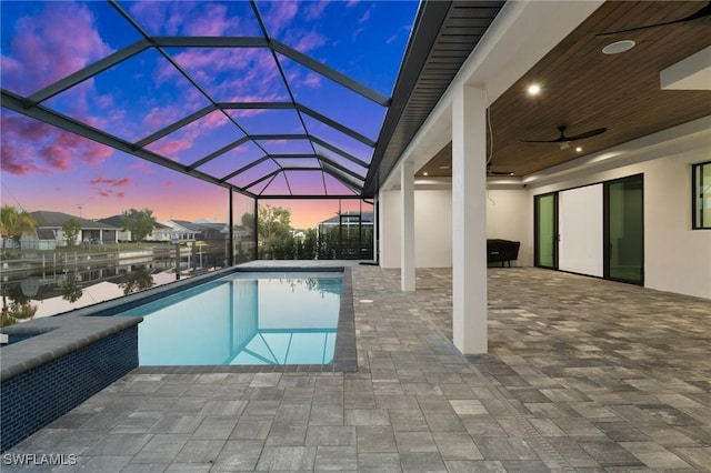 pool at dusk with a water view, a patio, a lanai, and ceiling fan