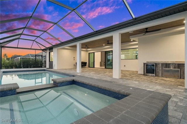 pool at dusk featuring an in ground hot tub, ceiling fan, a patio, and glass enclosure