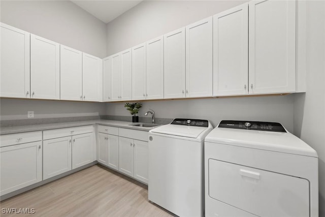 clothes washing area with cabinets, washing machine and clothes dryer, light hardwood / wood-style floors, and sink