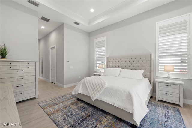 bedroom featuring multiple windows, light wood-type flooring, and a tray ceiling