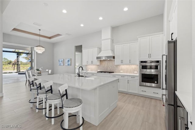 kitchen with sink, white cabinetry, appliances with stainless steel finishes, a raised ceiling, and a kitchen island with sink