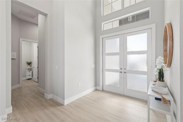 foyer with a high ceiling, light hardwood / wood-style flooring, and french doors