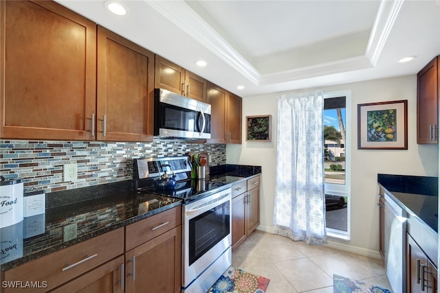 kitchen with light tile patterned floors, appliances with stainless steel finishes, backsplash, a raised ceiling, and dark stone counters