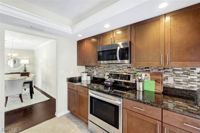 kitchen featuring light tile patterned flooring, dark stone countertops, decorative backsplash, ornamental molding, and stainless steel appliances