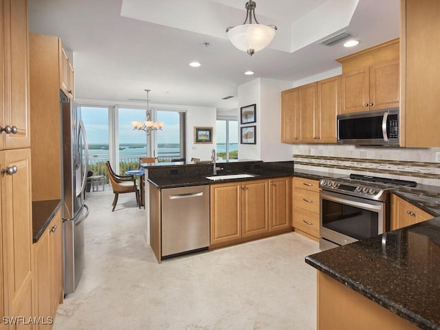 kitchen with a water view, dark stone countertops, appliances with stainless steel finishes, kitchen peninsula, and pendant lighting