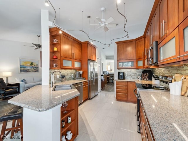 kitchen with sink, a breakfast bar, ceiling fan, appliances with stainless steel finishes, and light stone counters