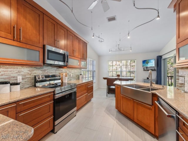 kitchen with vaulted ceiling, appliances with stainless steel finishes, sink, decorative backsplash, and light stone countertops