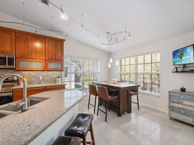 kitchen featuring sink, hanging light fixtures, light stone counters, tasteful backsplash, and vaulted ceiling