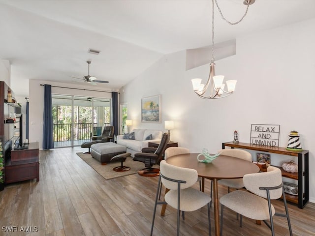 dining room with ceiling fan with notable chandelier, wood-type flooring, and vaulted ceiling