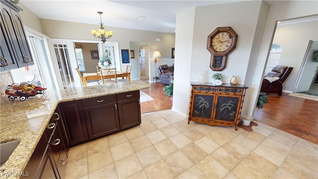 kitchen with hanging light fixtures, light stone counters, dark brown cabinetry, light hardwood / wood-style floors, and a chandelier