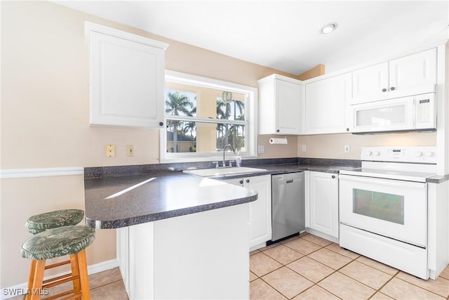 kitchen featuring sink, white appliances, white cabinetry, a kitchen bar, and kitchen peninsula