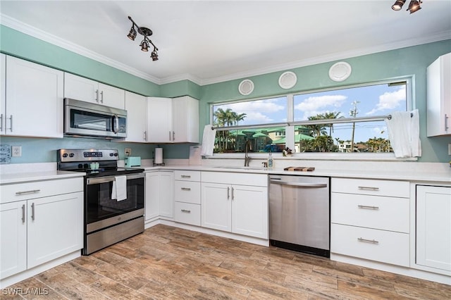 kitchen with sink, white cabinetry, ornamental molding, appliances with stainless steel finishes, and light hardwood / wood-style floors