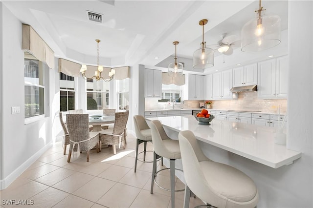 kitchen featuring white cabinets, decorative light fixtures, light tile patterned floors, and backsplash