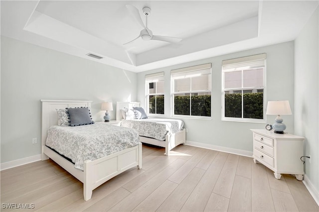 bedroom with light wood-type flooring, ceiling fan, and a tray ceiling